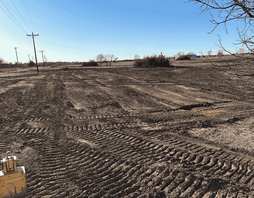 Close view of a cleared field dotted with uprooted cedar and oak brush piles, crisscrossed by dozer track marks.