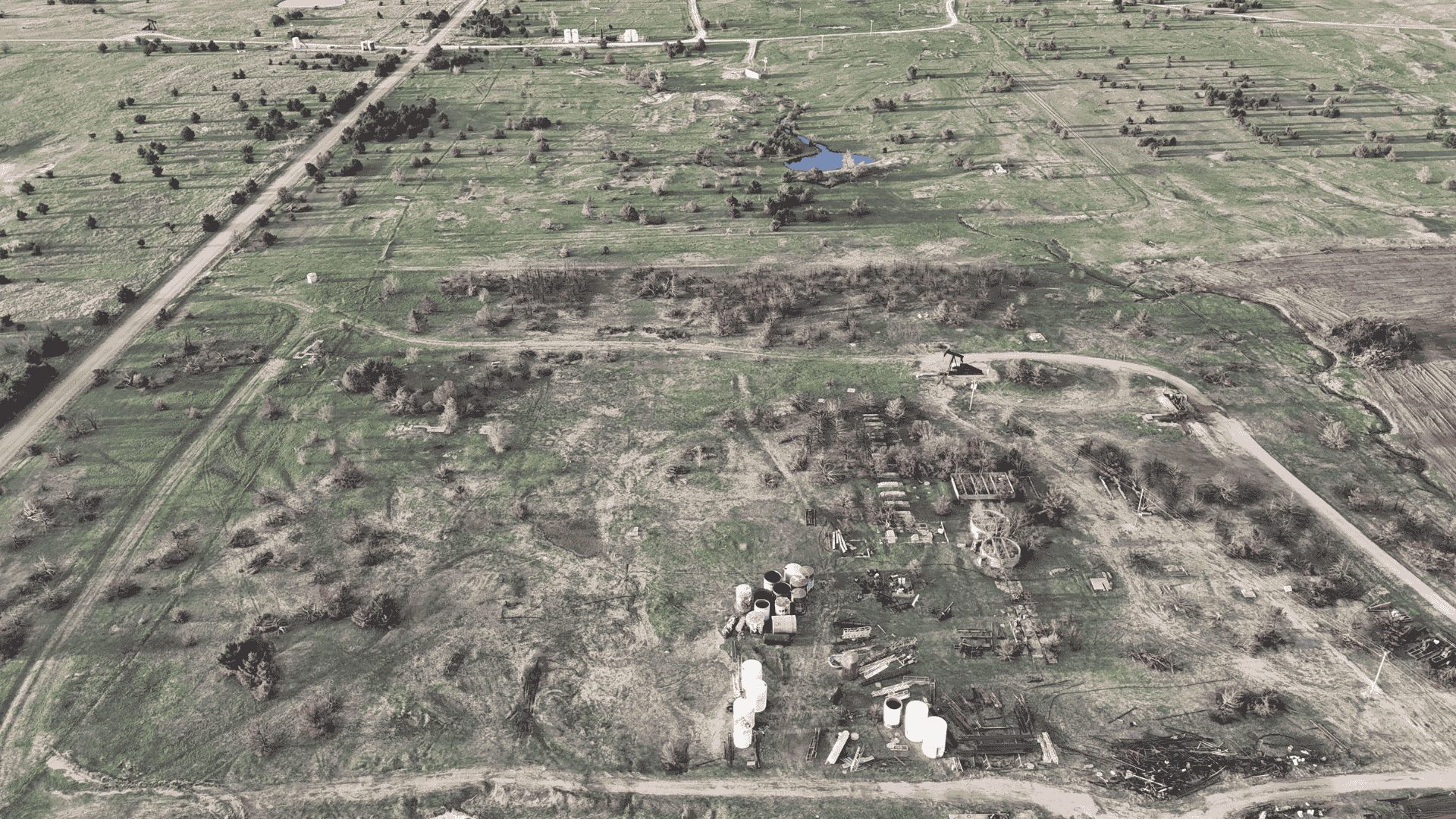 Wide aerial shot of a rural demolition site showing debris piles, uprooted brush, and earth-moving tracks