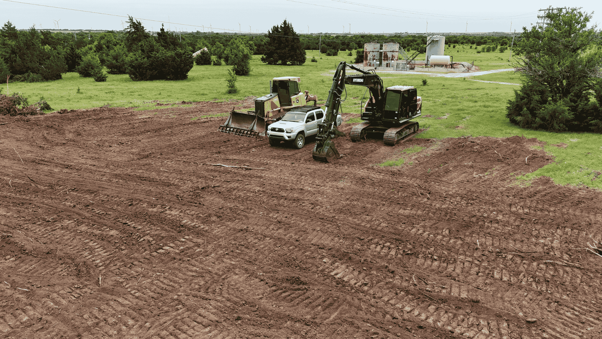 Bulldozer and excavator parked on freshly cleared terrain, surrounded by scattered tree stumps and brush
