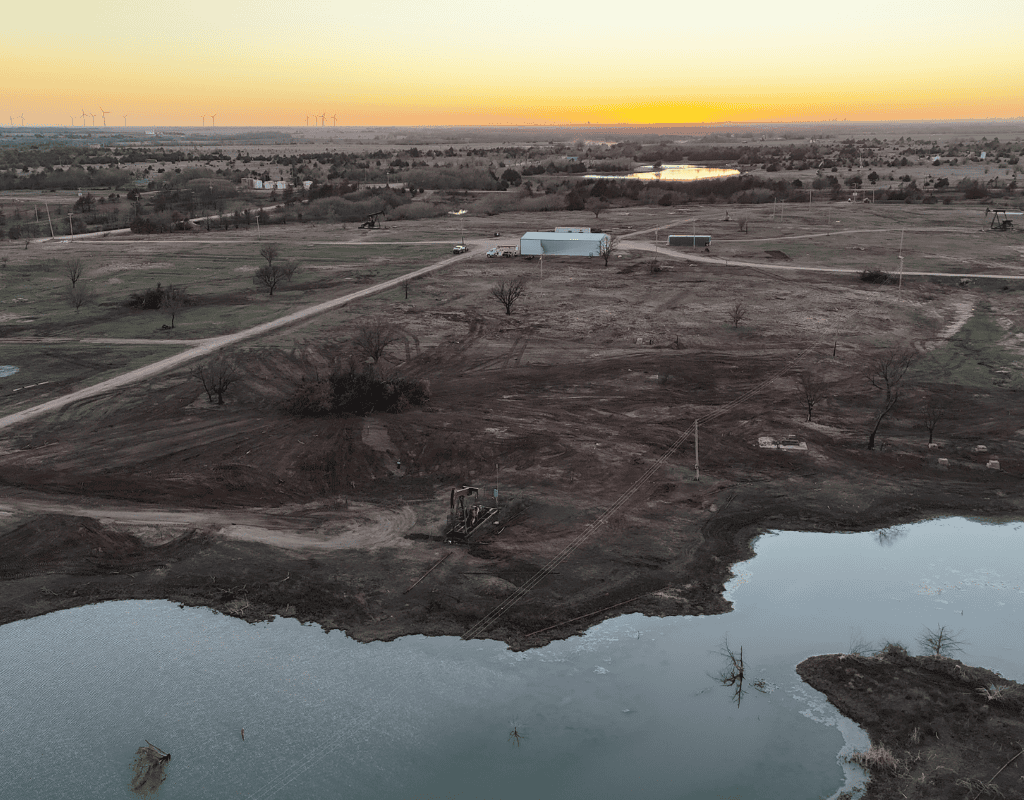 Sunset aerial panorama of a recently dug farm pond filling with water at the edge of cleared pasture, with the surrounding acreage freshly graded.
