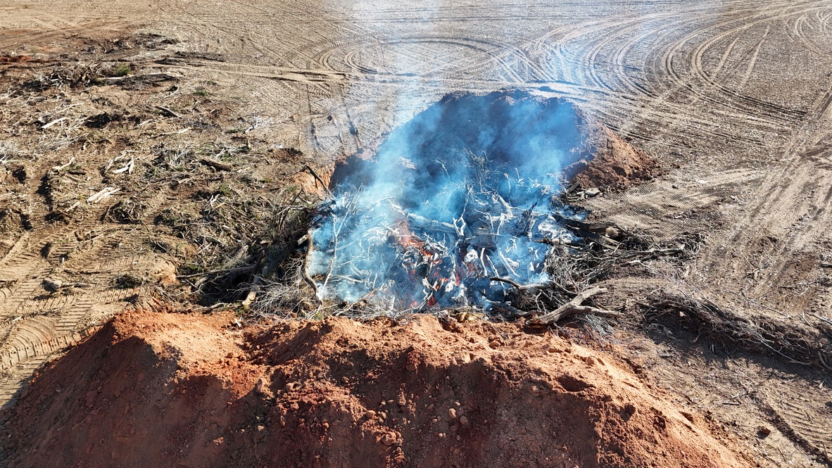 Large brush fire on cleared land with dirt mounds.