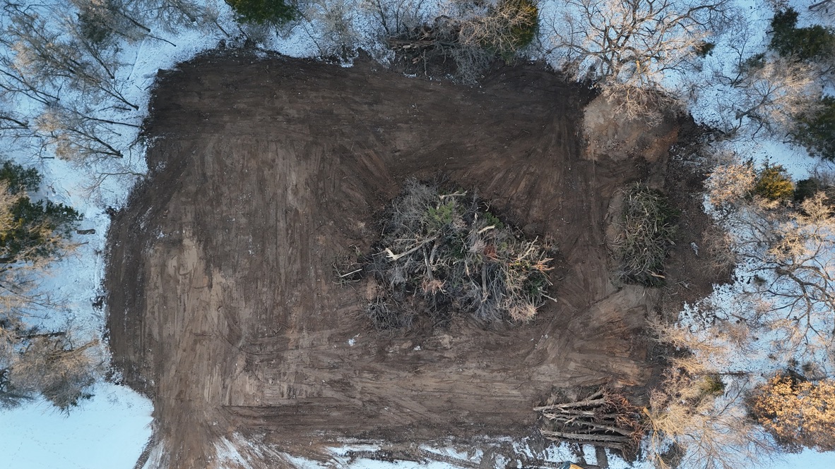 Aerial view of cleared dirt land and a large brush pile.