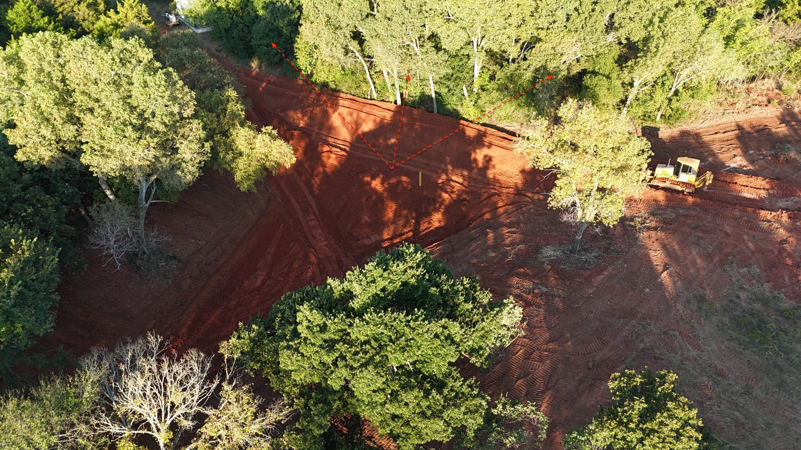 Aerial view of a bulldozer clearing red dirt in a forest.